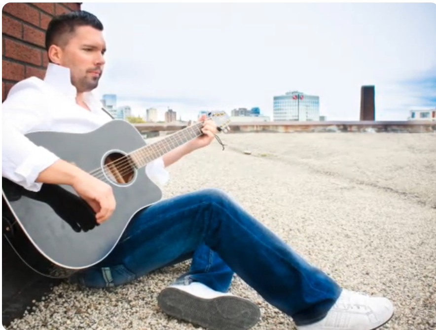 Earlier photograph playing acoustic guitar on a rooftop